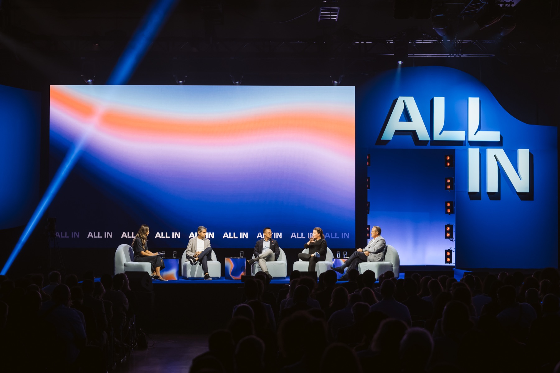 Wide view of the ALL IN stage with five panel participants and the audience